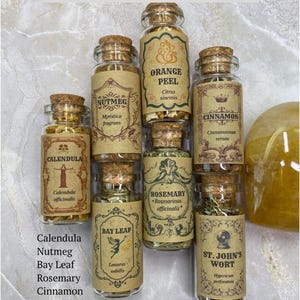 May include: Seven small glass jars with cork stoppers, each containing dried herbs or spices labeled Calendula, Nutmeg, Orange Peel, Cinnamon, Bay Leaf, Rosemary, and St. John's Wort. The set is titled LEO inspired collection - The RADIANT.