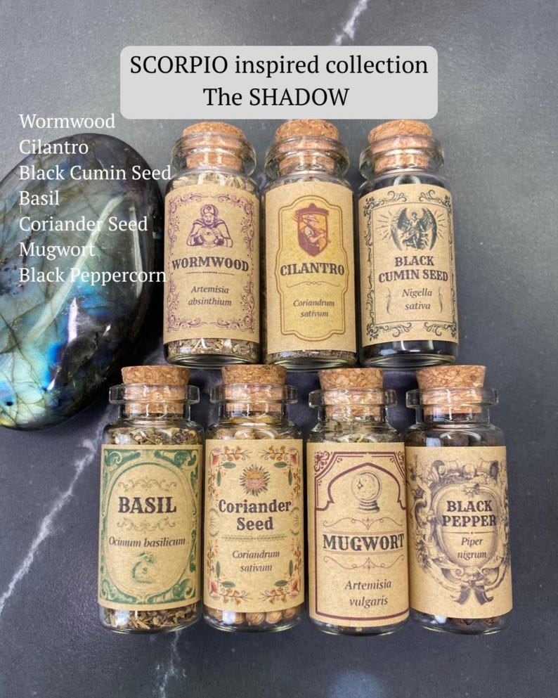 May include: A collection of seven small glass jars with cork stoppers, each containing dried herbs or seeds. Labels feature text: Wormwood, Cilantro, Black Cumin Seed, Basil, Coriander Seed, Mugwort, and Black Pepper. A large, iridescent stone sits to the left.