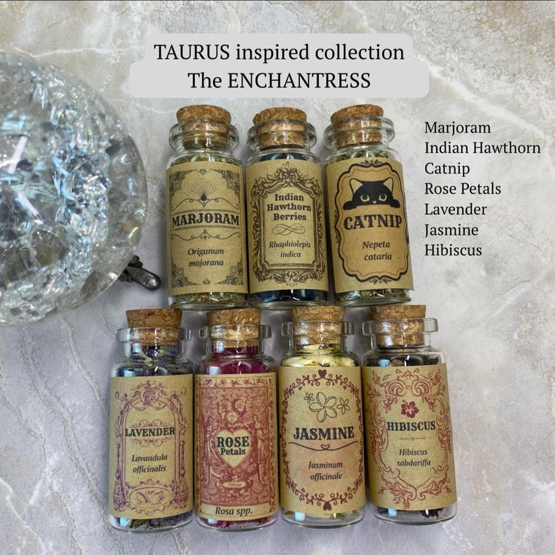 May include: Seven small glass jars with cork stoppers, each containing dried herbs and flowers. Labels read TAURUS inspired collection, The ENCHANTRESS, Marjoram, Indian Hawthorn Berries, Catnip, Lavender, Rose Petals, Jasmine, and Hibiscus.