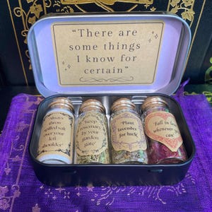 May include: A black tin box containing four small glass bottles with cork stoppers. Each bottle has a label with text. The box also contains a card with the quote "There are some things I know for certain."