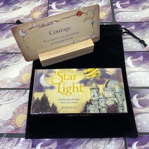 May include: A tarot card set with a card reading "Courage" and a wooden stand. Below is a box labelled "Star Light" with a castle illustration. The set is presented on a black velvet bag.