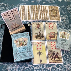 May include: A deck of Easy Lenormand cards by Marcus Katz and Tali Goodwin, featuring a box with the title and illustrations. Several cards are displayed, including one on a wooden stand showing a ship, and others depicting a snake, a book, a key, and a person on horseback.