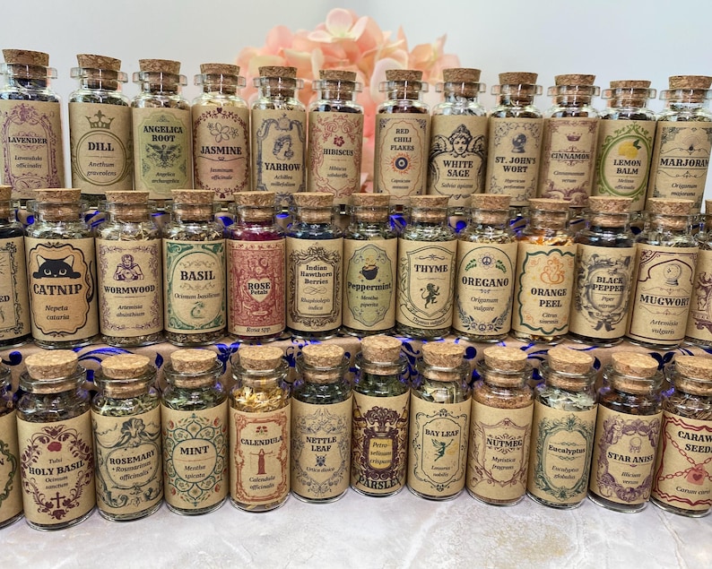 May include: A collection of small, clear glass apothecary jars with cork stoppers, each filled with dried herbs or spices. Every jar features a vintage-style tan paper label with ornate borders, botanical illustrations, and the name of the herb.