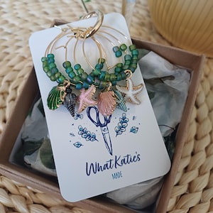 May include: Set of five gold hoop earrings with green beads and charms. The charms include a seashell, a starfish, and a small green shell. The earrings are packaged in a box with the text "What Katie's Made".