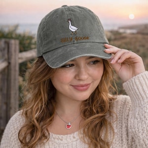 K&ouml;nnte beinhalten: Graue Baseballkappe mit dem gestickten Schriftzug "Silly Goose" und einem Enten-Cartoon-Design. Die Kappe besteht aus einem weichen, abgenutzten Material und hat einen gebogenen Schirm. Ein l&auml;ssiges Accessoire.