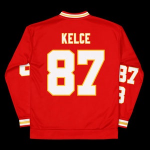 Puede incluir: Jersey rojo de manga larga con ribetes blancos y dorados. El jersey tiene el nombre "KELCE" y el n&uacute;mero "87" en la espalda.