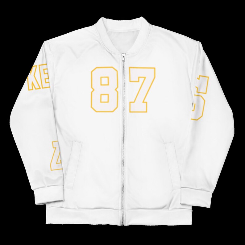 Puede incluir: Chaqueta bomber blanca con cierre de cremallera. La chaqueta tiene el n&uacute;mero "87" impreso en la parte delantera con contorno amarillo. El n&uacute;mero "8" est&aacute; impreso en la manga izquierda y el n&uacute;mero "5" est&aacute; impreso en la manga derecha, tambi&eacute;n con contorno amarillo.