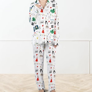 Può includere: Pigiama bianco con un motivo ripetuto di illustrazioni a tema natalizio, tra cui cappelli di Babbo Natale, luci natalizie e figure danzanti. Il set comprende una camicia con colletto abbottonata e pantaloni abbinati.