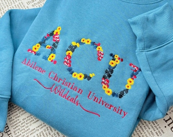 May include: A light blue sweatshirt with the text "ACU Abilene Christian University Wildcats" embroidered in yellow, red, and green flowers.