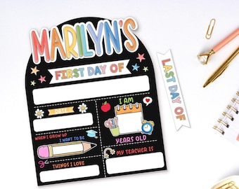 May include: A black chalkboard-style sign with the text "MARILYN'S FIRST DAY OF" in colorful letters. The sign includes spaces for information, along with illustrations of a pencil, apple, and clock. A separate "LAST DAY OF" tag is also present.