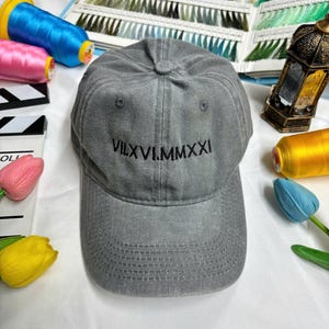 May include: A gray baseball cap with a black embroidered design that reads "VII.XVI.MMXXI".