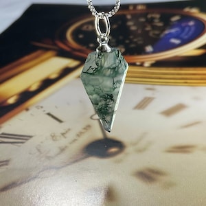May include: A silver chain necklace with a green moss agate pendant in the shape of a point. The pendant is faceted and has a silver bail.
