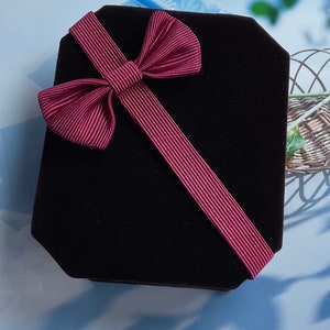 May include: A black velvet gift box with a burgundy ribbon tied in a bow.