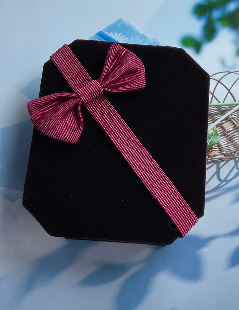 May include: A black velvet gift box with a burgundy ribbon tied in a bow.