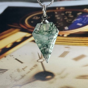 May include: A silver chain necklace with a green moss agate pendant in the shape of a diamond. The pendant is clear with green moss-like inclusions.