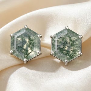 Könnte beinhalten: Ein Paar hexagonale Ohrstecker mit durchscheinenden Moosachat-Steinen und komplexen grünen dendritischen Einschlüssen, die jeweils sicher in einer polierten silberfarbenen Metallfassung mit sechs Krappen gehalten werden.