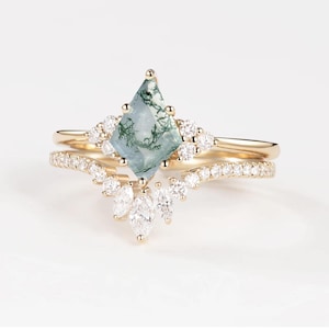 May include: A two-piece gold ring set. The engagement ring features a light blue, diamond-shaped stone with green inclusions, surrounded by small, clear stones. The band is a simple gold band. The wedding band is a curved gold band with small, clear stones.