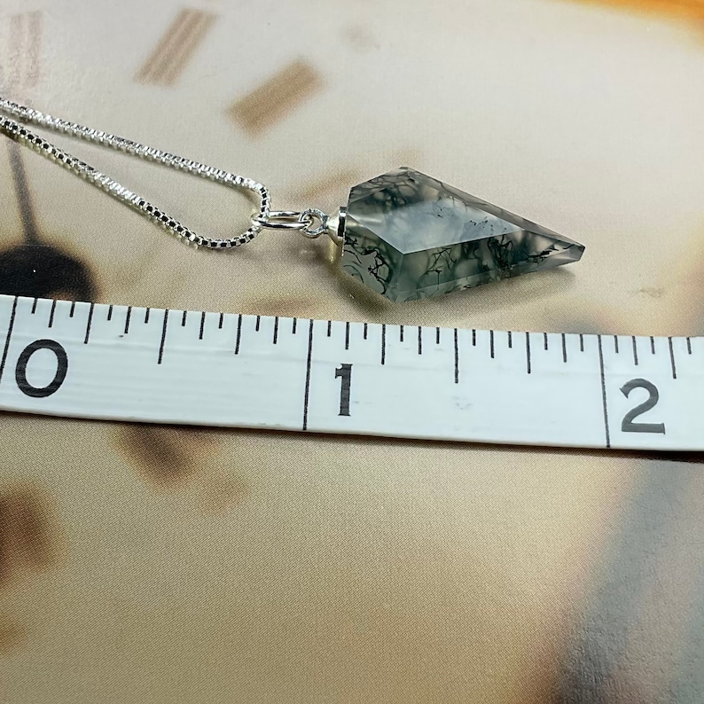 May include: A silver chain necklace with a grey and black dendritic agate pendant shaped like a point. The pendant is approximately 2.5 cm long.