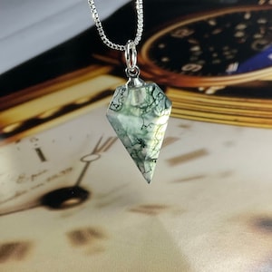 May include: A silver chain necklace with a green moss agate pendant shaped like a diamond. The pendant is translucent and has a natural, organic pattern.