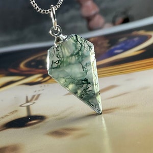 May include: A silver chain necklace with a green moss agate pendant in the shape of a point.