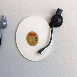 May include: A white vinyl record with a Soundgarden label is mounted on a wall. A black turntable arm and a silver knob are visible. The record player is a decorative item.