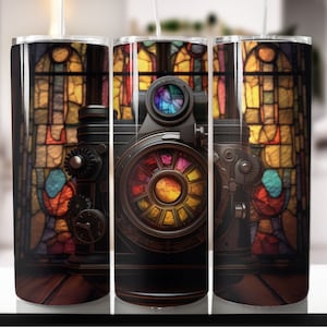 May include: A vintage-style camera with a colorful, circular lens sits in front of a stained glass window. The camera is made of metal and has a black finish. The stained glass window is colorful and has a variety of shapes and designs.