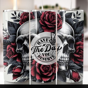 Peut inclure: Un gobelet blanc avec un motif de crâne et de roses. Le crâne a un signe de paix sur un œil. Le texte sur le gobelet est "Have The Day You Deserve".