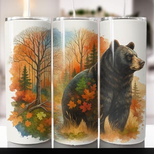 Peut inclure: Un gobelet blanc avec une illustration à l'aquarelle d'un ours noir dans une forêt. Le motif comprend un feuillage d'automne aux tons orange, rouge et vert, avec un arbre nu et une forêt en arrière-plan. Le gobelet est cylindrique.