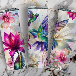 May include: Three stainless steel tumblers with colorful hummingbird and floral designs. The tumblers are white with a watercolor-like effect. The flowers are pink, purple, and white. The hummingbirds are blue, green, and purple.