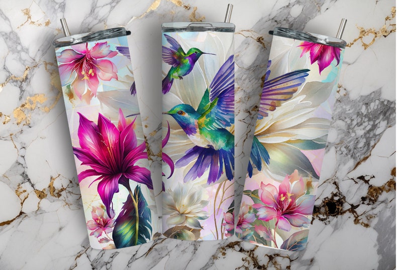 May include: Three stainless steel tumblers with colorful hummingbird and floral designs. The tumblers are white with a watercolor-like effect. The flowers are pink, purple, and white. The hummingbirds are blue, green, and purple.
