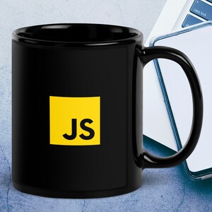 Op de afbeelding: Zwarte keramische koffiemok met een geel vierkant met de letters "JS" in zwart.