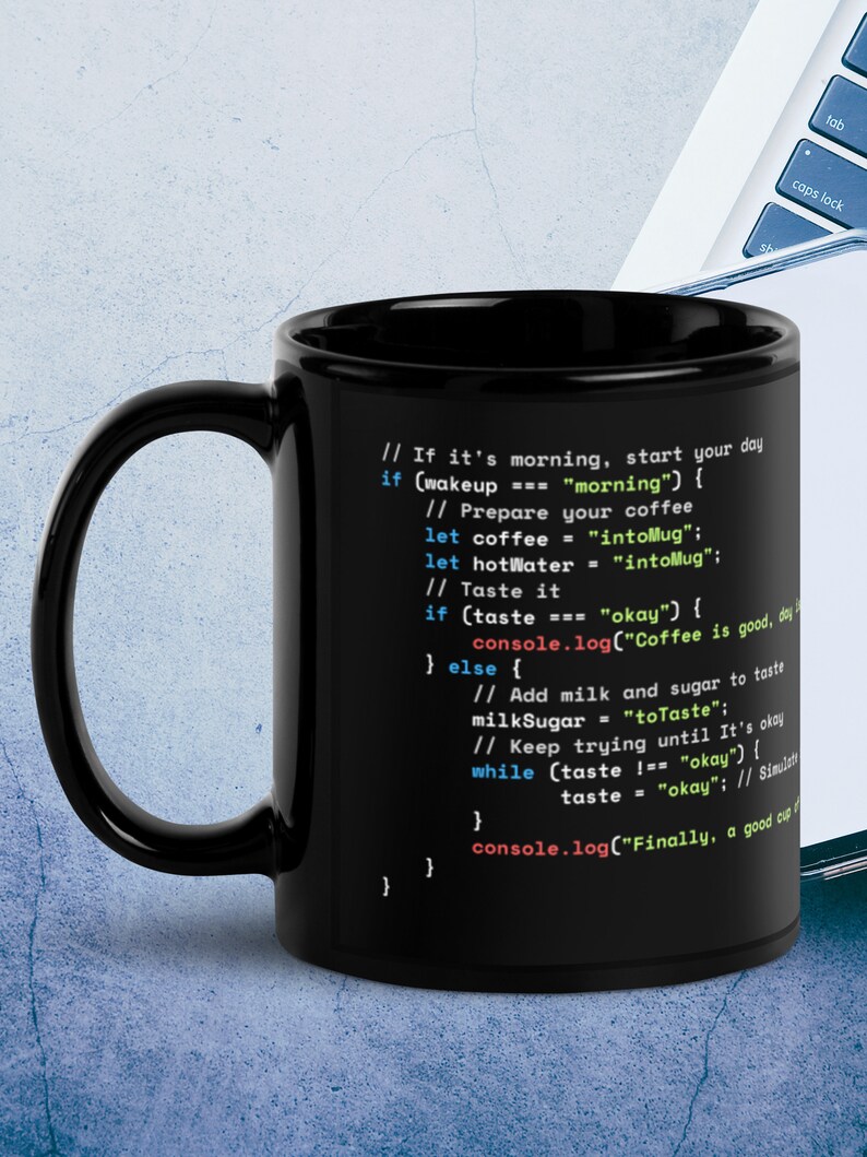Op de afbeelding: Zwarte koffiemok met een wit ontwerp van code die "If it's morning, start your day. If (wakeup === "morning") { // Prepare your coffee let coffee = "intoMug"; let hotWater = "intoMug"; // Taste it if (taste === "okay") { console.log("Coffee is good, day } else { // Add milk and sugar to taste milkSugar = "toTaste"; // Keep trying until It's okay while (taste !== "okay") { taste = "okay"; // Simulati console.log("Finally, a good cup"