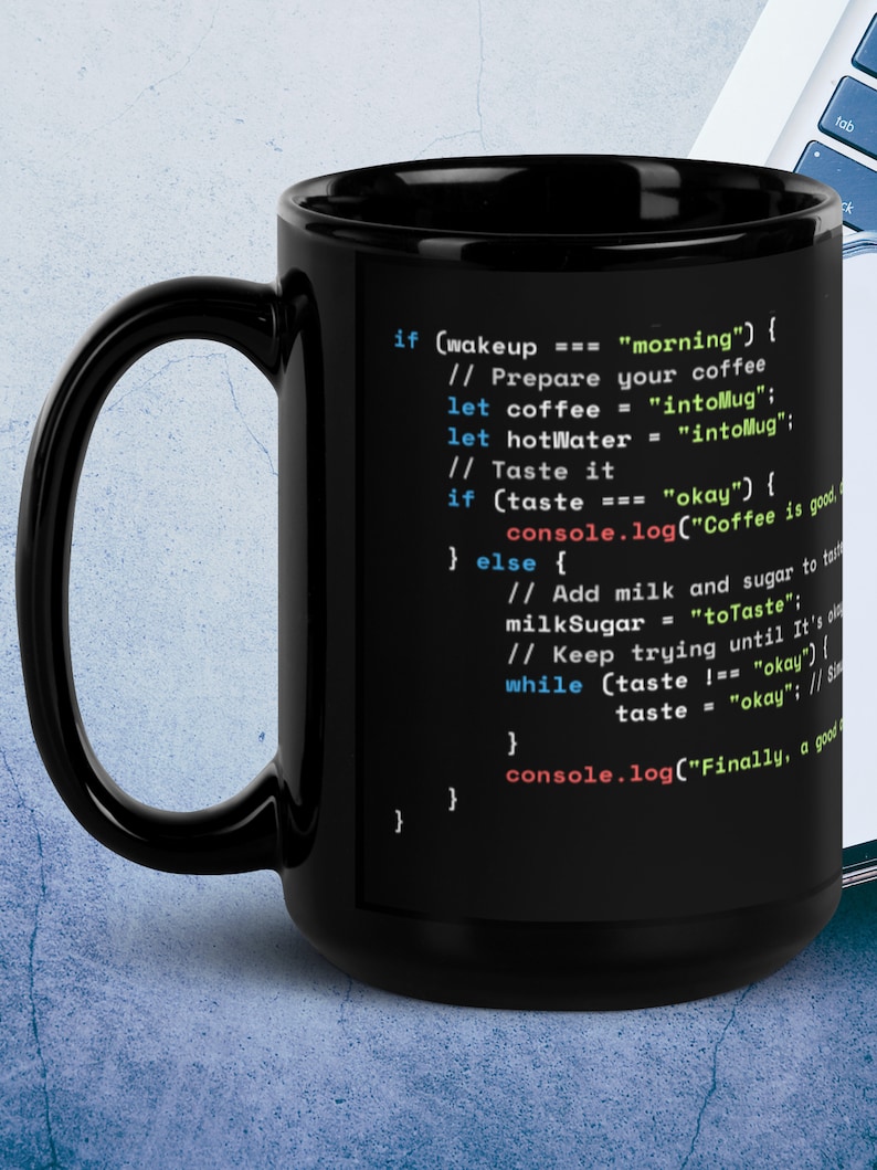 Op de afbeelding: Een zwarte koffiemok met een wit ontwerp met code die luidt "if (wakeup === "morning") { // Prepare your coffee let coffee = "intoMug"; let hotWater = "intoMug"; // Taste it if (taste === "okay") { console.log("Coffee is good"); } else { // Add milk and sugar to taste milkSugar = "toTaste"; // Keep trying until it's also okay while (taste !== "okay") { taste = "okay"; // Since it's also okay console.log("Finally, a good cup of coffee"); } } }"