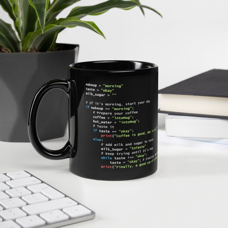 May include: Black coffee mug with a Python code snippet printed on the side. The code includes phrases like "morning", "okay", and "intoMug". The mug is on a white surface with a keyboard and a plant in the background.