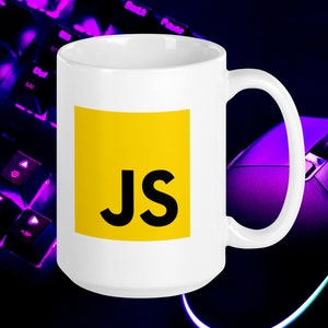 Pu&ograve; includere: Una tazza in ceramica bianca con un quadrato giallo che presenta le lettere "JS" in nero. La tazza &egrave; su una superficie nera con una tastiera e un mouse viola sullo sfondo.