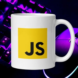 Pu&ograve; includere: Una tazza in ceramica bianca con un quadrato giallo che presenta il testo "JS" in nero. La tazza &egrave; su una tastiera e un mouse viola.