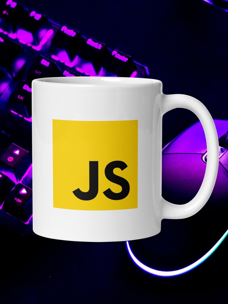 Pu&ograve; includere: Una tazza in ceramica bianca con un quadrato giallo che presenta il testo "JS" in nero. La tazza &egrave; su una tastiera e un mouse viola.