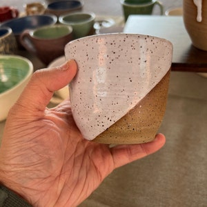 May include: A white and brown speckled ceramic mug with a white glaze on the top half and a brown glaze on the bottom half.