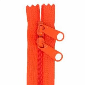 Puede incluir: Una cremallera de color naranja brillante con dos tiradores. La cremallera está cerrada y lista para ser cosida en una prenda o proyecto.