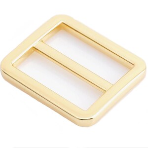 May include: A gold-colored metal buckle with a rectangular shape and a single, horizontal slot.