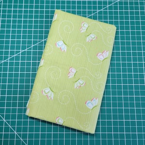 May include: A green fabric with a white and pink butterfly pattern. The fabric has a subtle striped texture.