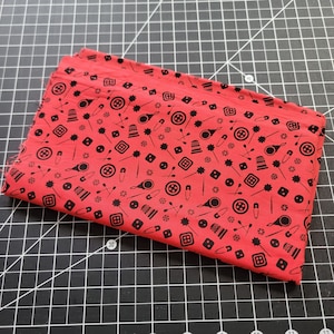 May include: Red fabric with a black and white repeating pattern of sewing-related items, including needles, thread, buttons, and thimbles.