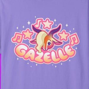 May include: A lilac-colored t-shirt featuring a cartoon gazelle design. The gazelle has tan fur, a blonde side-swept bang, and is surrounded by musical notes and stars. The word "GAZELLE" is written in a bubble font.