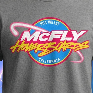 May include: A heather gray t-shirt featuring a retro design for "McFly Hoverboards" with a blue, pink, and yellow logo. The design includes the text "Hill Valley" and "California".