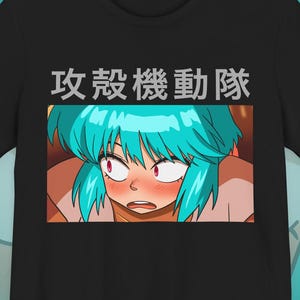 Könnte beinhalten: Ein schwarzes Kurzarm-T-Shirt mit einer rechteckigen Grafik eines Anime-Charakters mit türkisfarbenem Haar und roten Augen. Über der Grafik ist der japanische Text 攻殻機動隊 in hellgrauer Schrift gedruckt. Der Charakter hat einen überraschten Ausdruck.