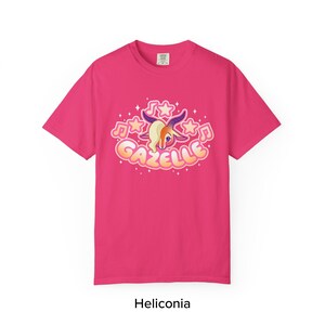 May include: A magenta t-shirt featuring a cartoon gazelle design with musical notes and stars. The gazelle has a cream-colored mane and purple horns. The word "Gazelle" is written in a bubble font. The text "Heliconia" is at the bottom.