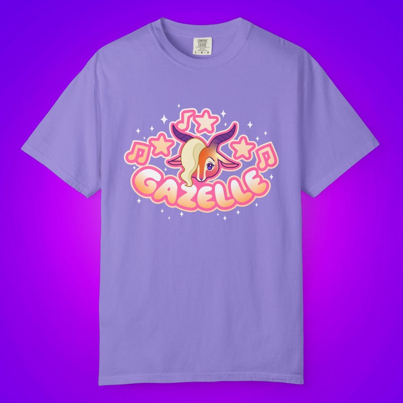 May include: A lilac-colored t-shirt featuring a cartoon gazelle design. The gazelle has tan fur, a blonde side-swept bang, and is surrounded by musical notes and stars. The word "GAZELLE" is written in a bubble font.