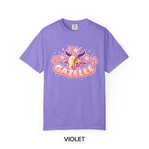 May include: Violet-colored t-shirt with a cartoon gazelle graphic. The graphic features a gazelle head with musical notes and stars, and the word "GAZELLE" in a bubble font. The word "VIOLET" is printed at the bottom.