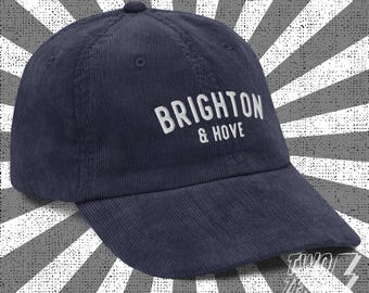 May include: A navy blue corduroy baseball cap with white embroidery that reads "BRIGHTON & HOVE".