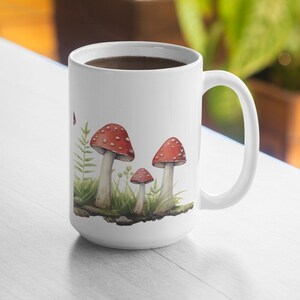 May include: White ceramic mug with a red and white mushroom illustration. The mug is filled with coffee and has a handle.